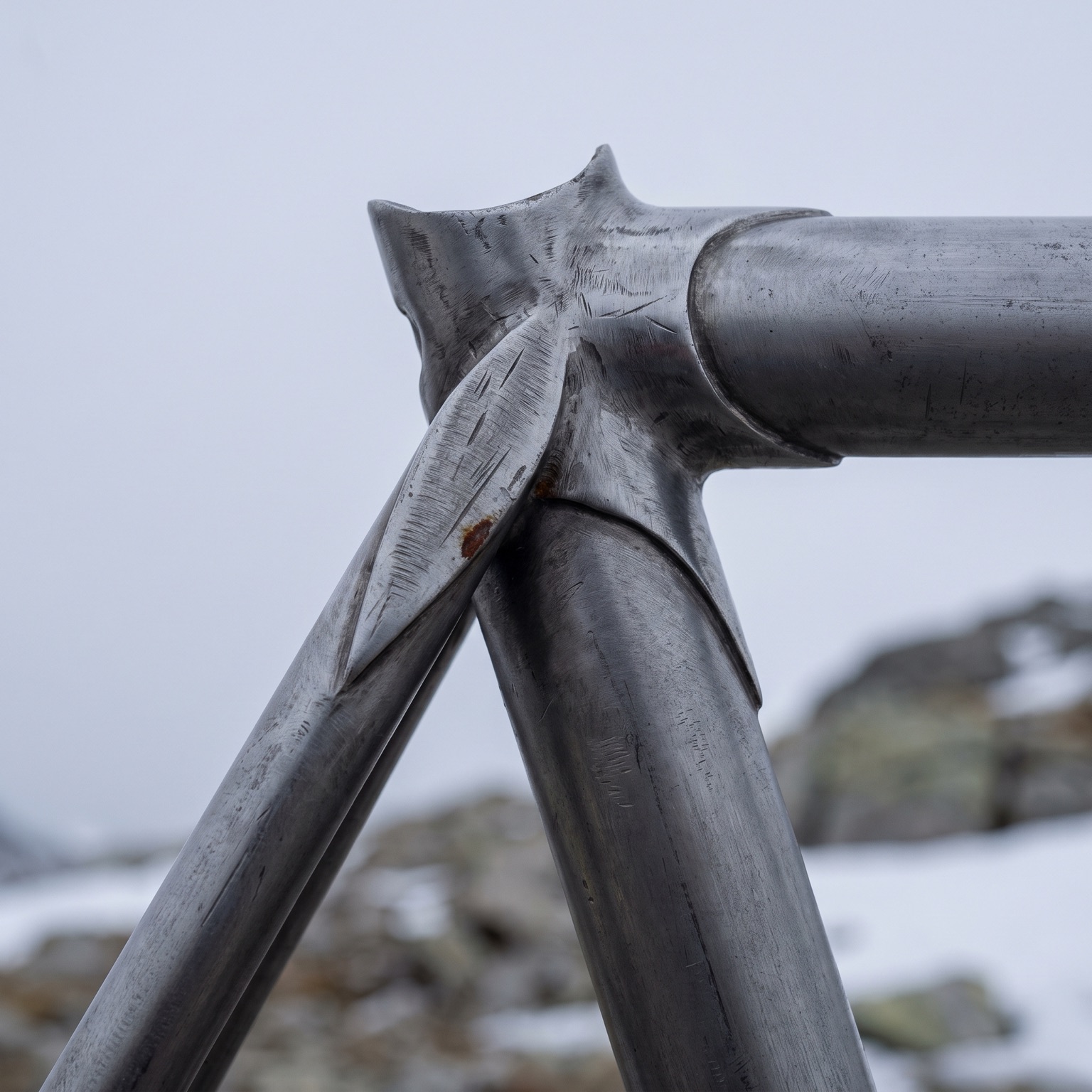 Extreme close-up of a hand-cut steel lug, filed into a tapering spearpoint where two tubes meet.